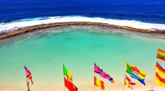 Vue aérienne d'un lagon turquoise protégé par une barrière de corail à La Réunion avec drapeaux de signalisation sur la plage