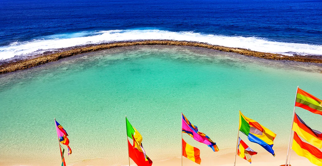 Vue aérienne d'un lagon turquoise protégé par une barrière de corail à La Réunion avec drapeaux de signalisation sur la plage