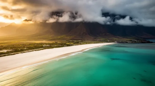 Vue aérienne de la côte ouest de La Réunion baignée de soleil avec le contraste des nuages sur les hauteurs