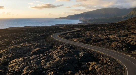 Vue panoramique de la route des laves traversant le paysage volcanique noir contrastant avec l'océan bleu à La Réunion