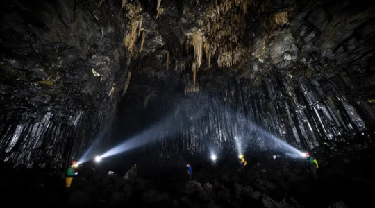 Vue à l'intérieur d'un tunnel de lave éclairé par des lampes frontales révélant les formations rocheuses volcaniques