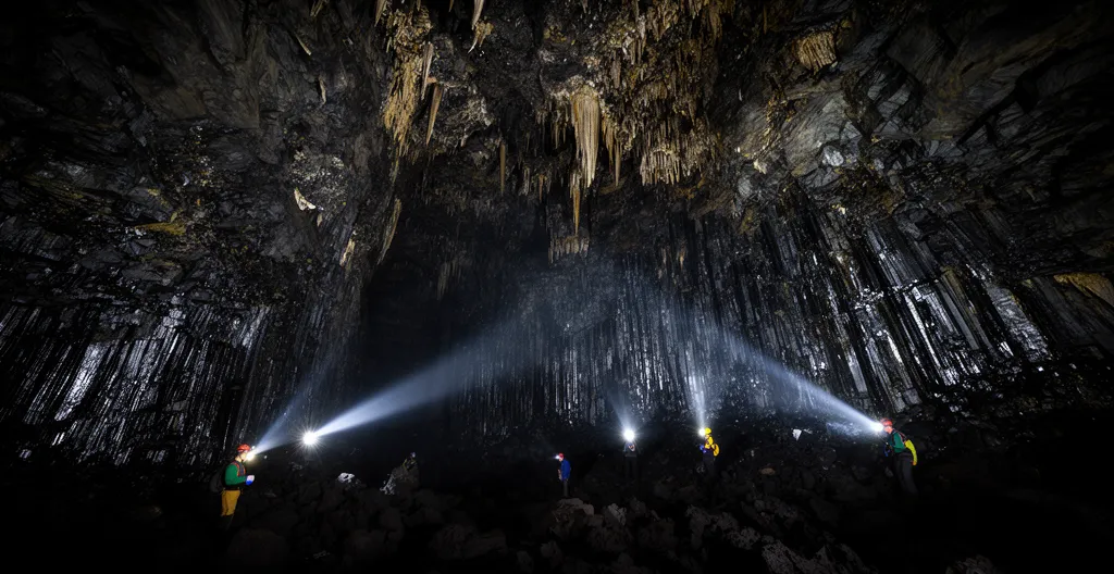 Vue à l'intérieur d'un tunnel de lave éclairé par des lampes frontales révélant les formations rocheuses volcaniques