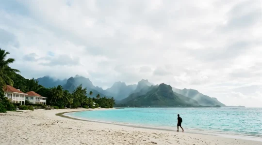 Vue panoramique d'une plage de sable blanc avec lagons turquoise et montagnes volcaniques à l'arrière-plan, représentant le paradis tropical européen de La Réunion